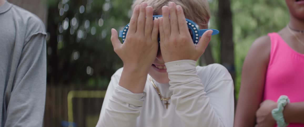 The video features a blonde boy wearing blue sharkthemed goggles looking forward with a serious expression then breaking into a smile he is wearing a white tshirt and a gold chain with a cross pendant