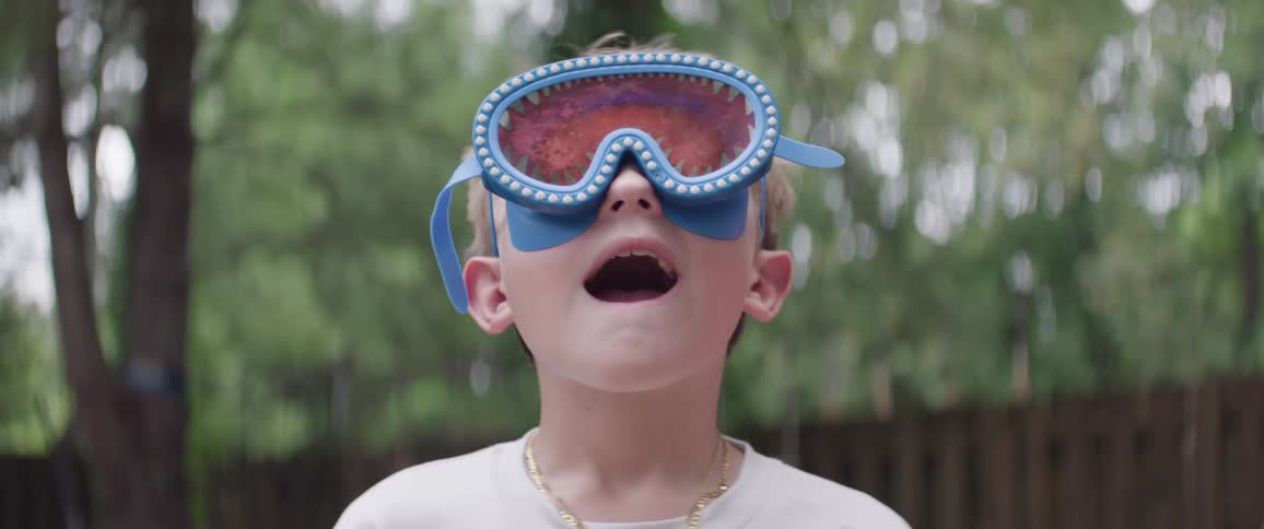 A young boy wearing playful sharkthemed swim goggles gazes upward with wideeyed wonder his mouth slightly open in awe