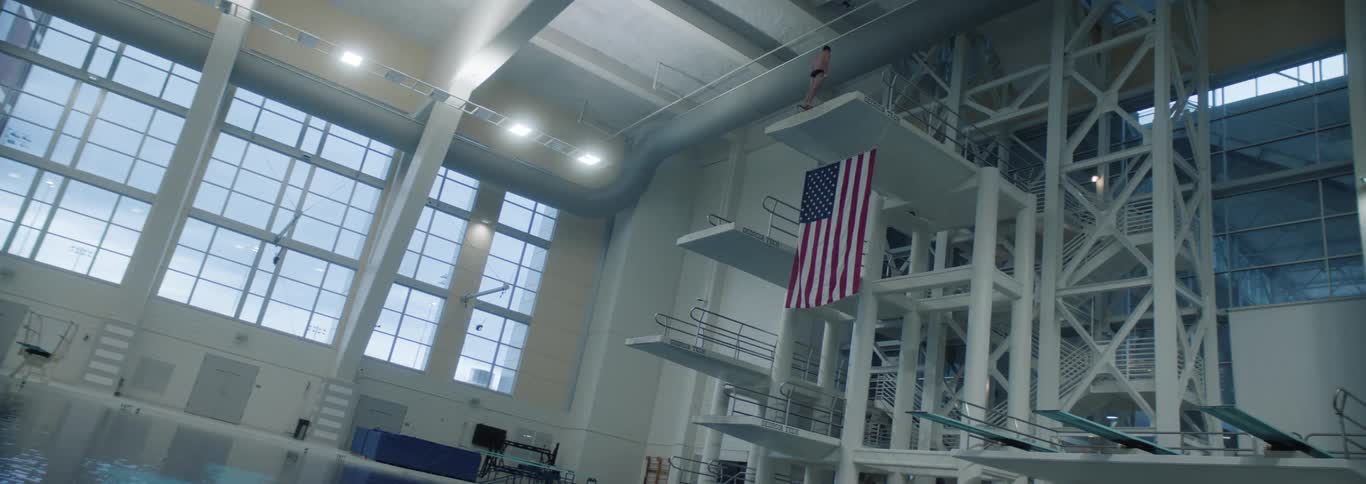 The diver stands on the diving platform with an american flag hanging from it