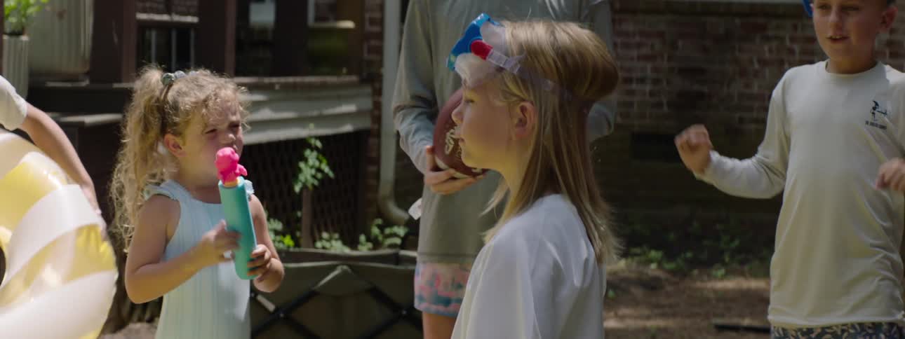 Little blonde girl with her eyes closed concentrating while other children around her jump and cheer happily as they watch