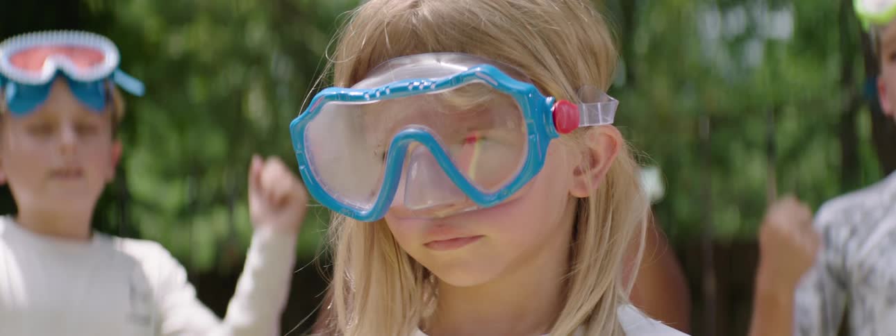 Concentrated blond child with glasses on side and other children in the background cheering happily