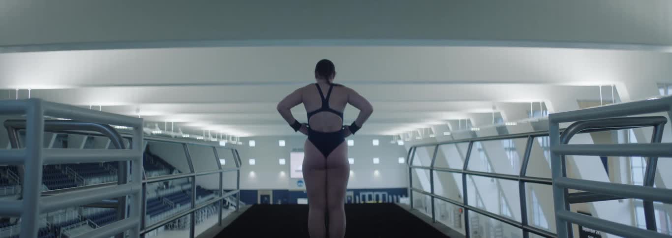 The swimmer walks to the edge of the diving platform and tosses a towel down
