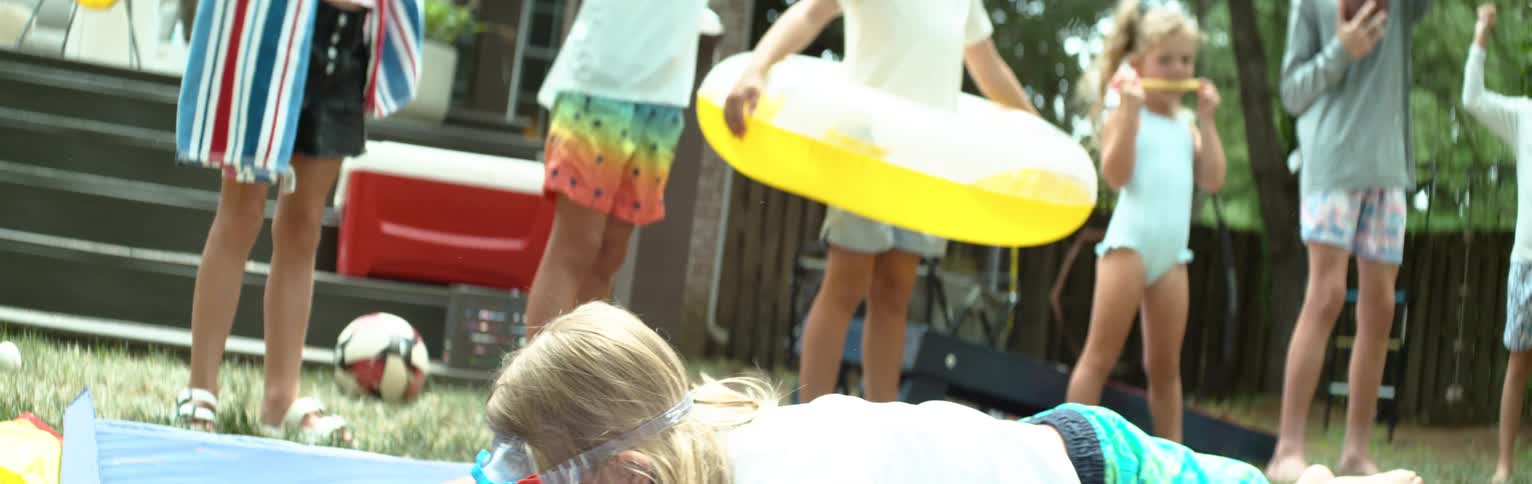 Several children watch and cheer as a boy is on a slipandslide