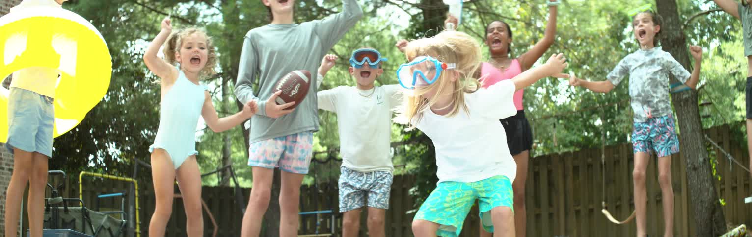 Little blonde girl running and playing in a backyard while her friends jump and cheer happily watching