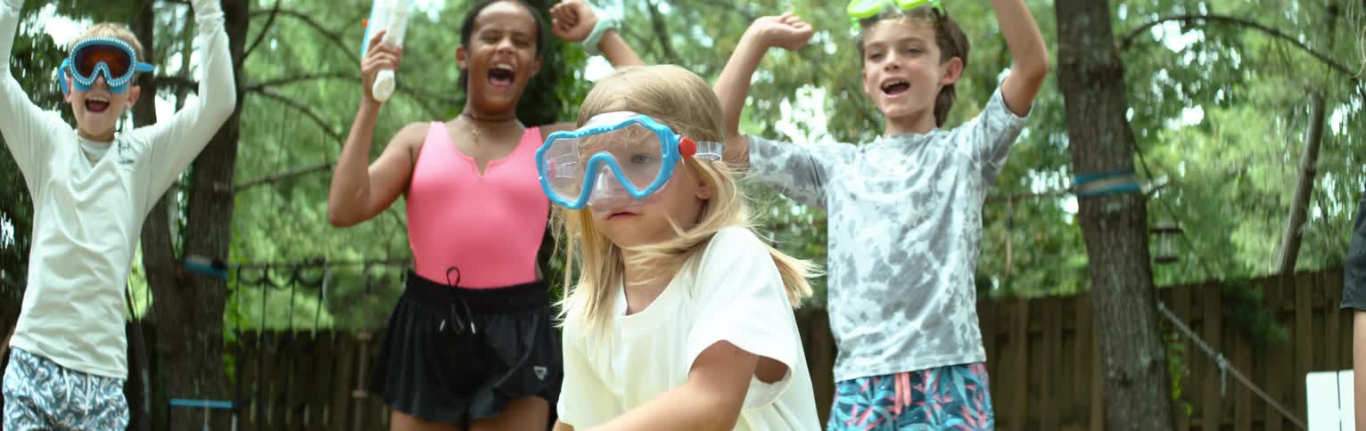A child wearing goggles runs in slow motion as her friends cheer her on from behind