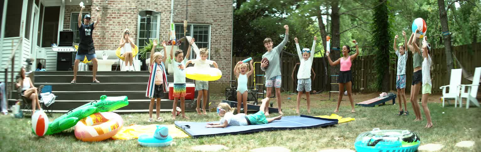 Group of children jumping happily and cheering as a little girl jumps and lands on a tarp in a backyard