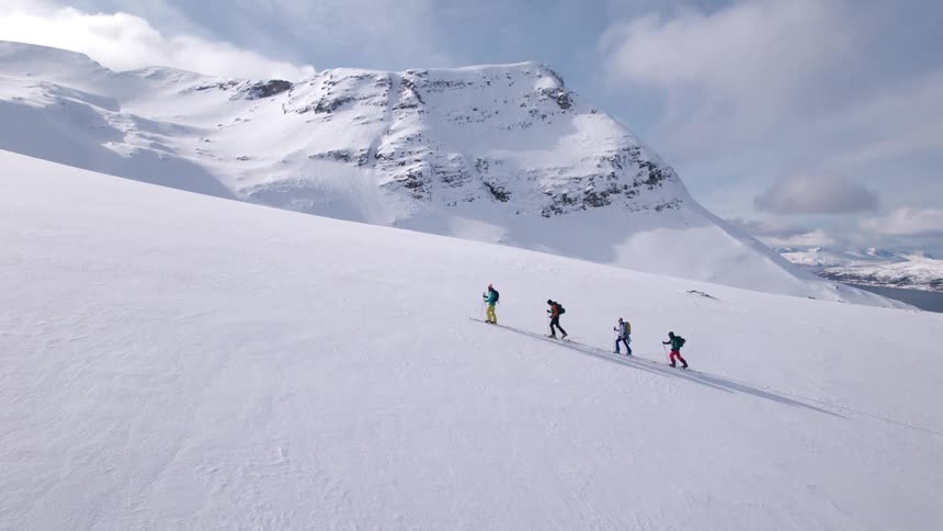 Skiers walk up a snow covered slope overlooking a river on a cloudy winter day