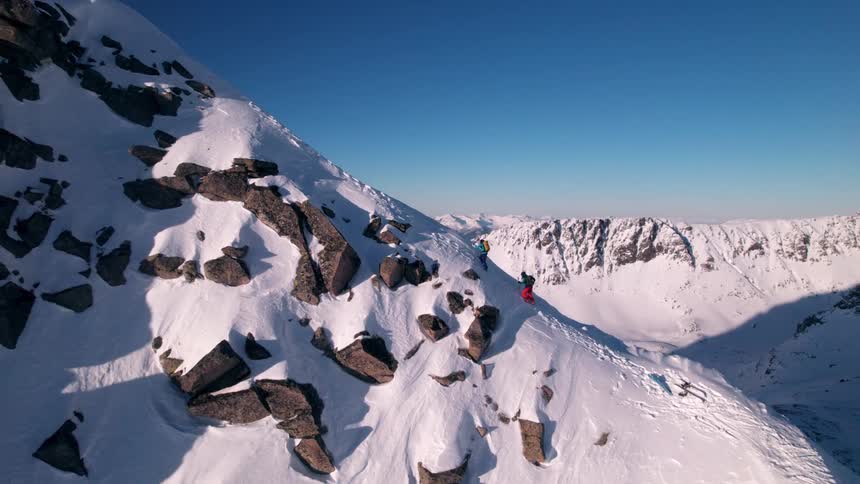 Two people hike up a snowcovered mountain at midday during the winter season on a sunny day