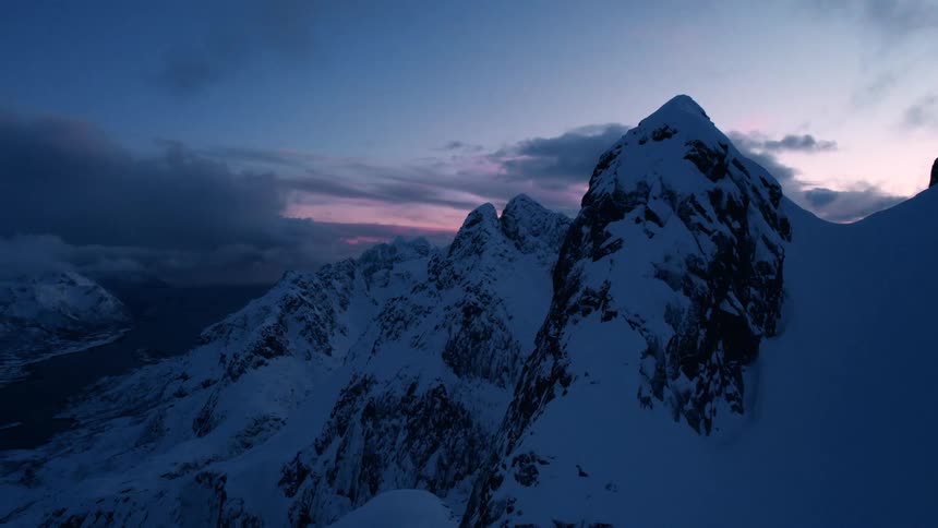 The video displays a dramatic landscape featuring towering snowcapped mountains under a twilight sky the sky transitions from dark blue at the top to hues of pink and purple near the horizon suggesting either sunrise or sunset