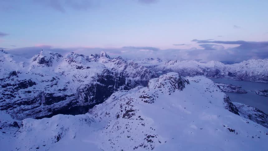 Snow covers the mountainous terrain surrounding a lake while red tints the clouds