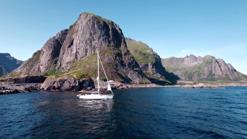 A sailboat is docked near the shore beside a rocky island at midday