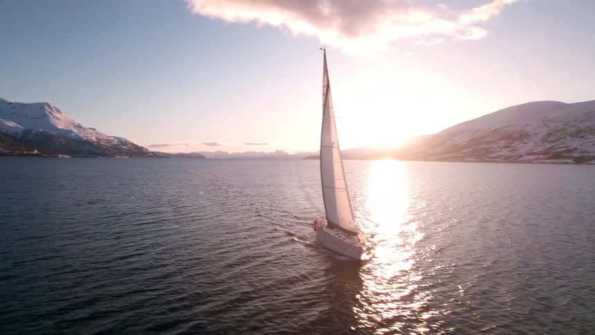 The sailboat is traveling in the water by the mountains