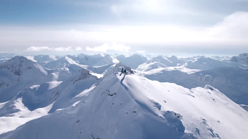 Two people reach the peak of an icy mountain at midday during winter