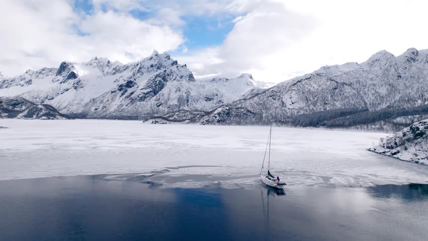 People stand on a sailboat partially sitting in frozen water on a cloudy winter day