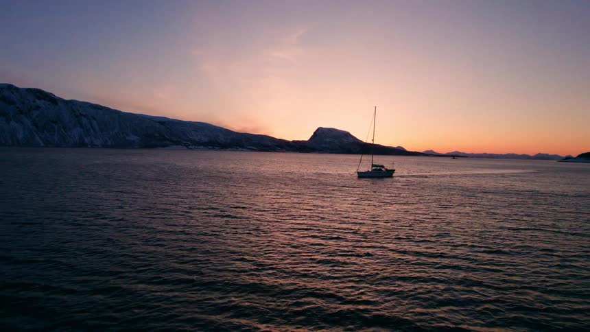 Sailboat at sunset with calm water and snowy mountains
