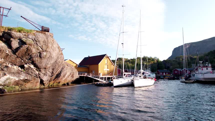 Sailboats docked at a coastal marina near cliffs and colorful houses