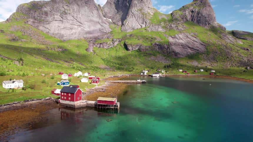 Village with small houses on the edge of a greenish lake and surrounded by mountains