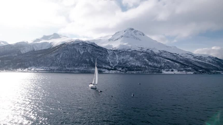 Sailboat traveling across the ocean with snowcovered mountains in the background
