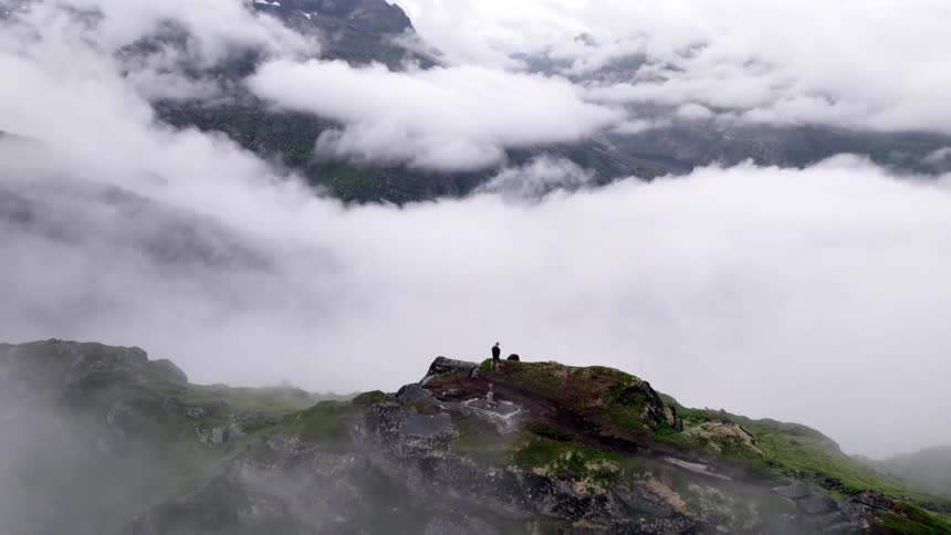A person hikes to the peak of a mountain in a foggy atmosphere at midday