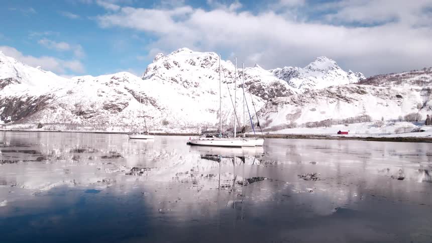 Sailboats on icy fjord amid snowy mountains