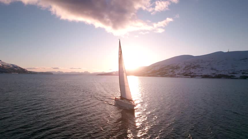 Sailboat traveling across the sea with mountains in the background