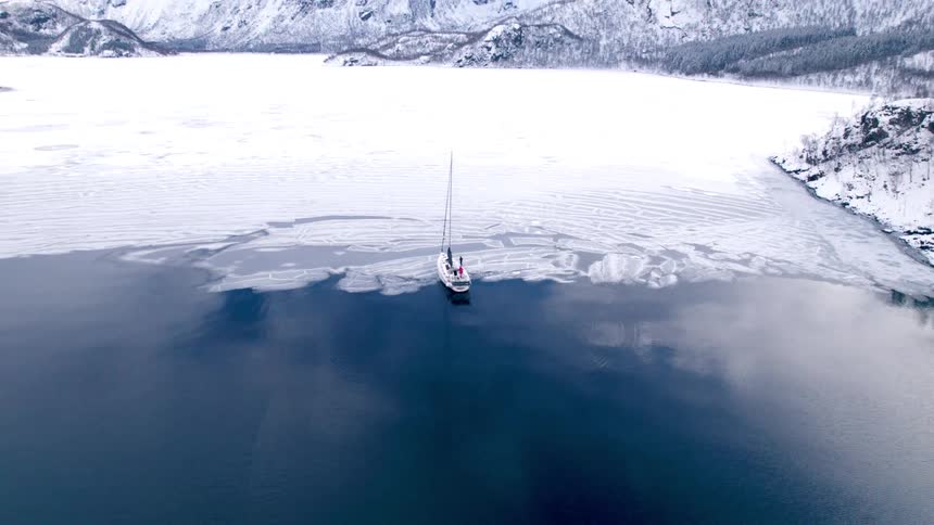 A person stands on a small sailboat in the ice of the lake