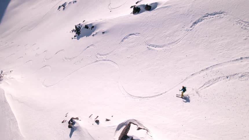 A skier carves down a snowy mountain slope beneath clear skies