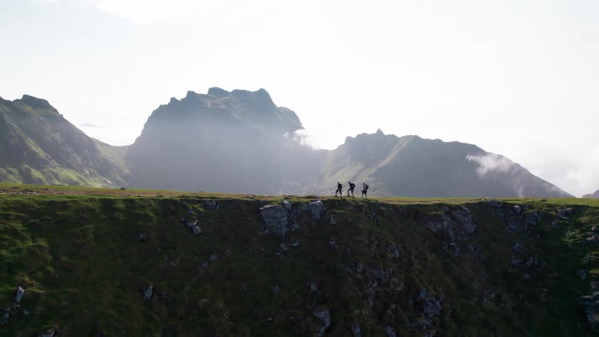 People are hiking on the green mountain on a foggy day