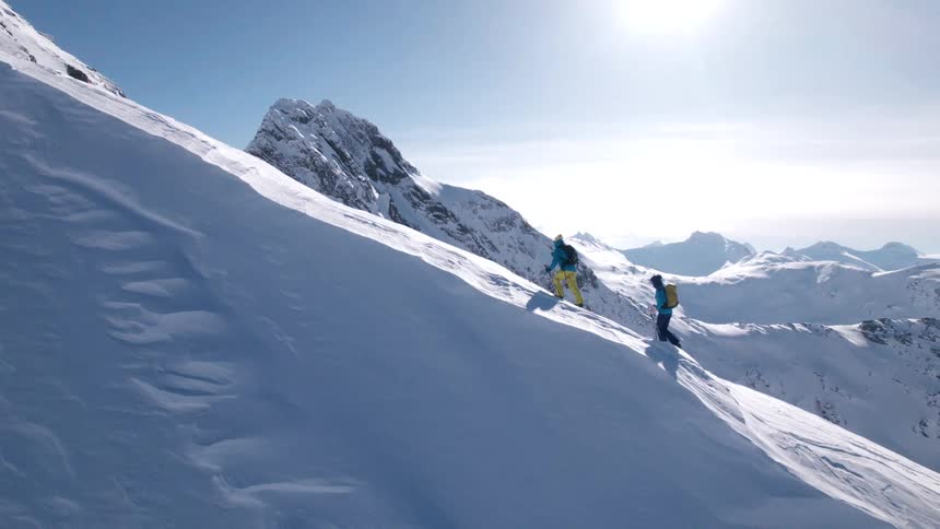 The two snow skiers are climbing up to the summit of the mountain