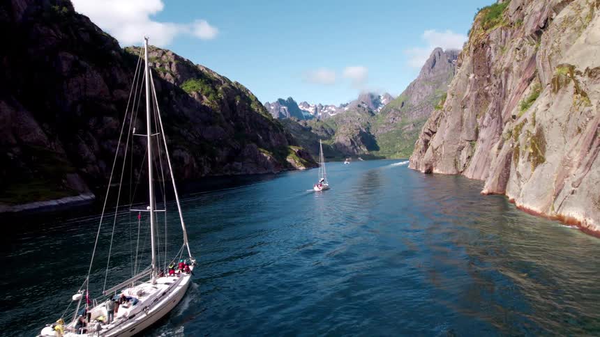 Sailboats traveling across the ocean surrounded by mountains
