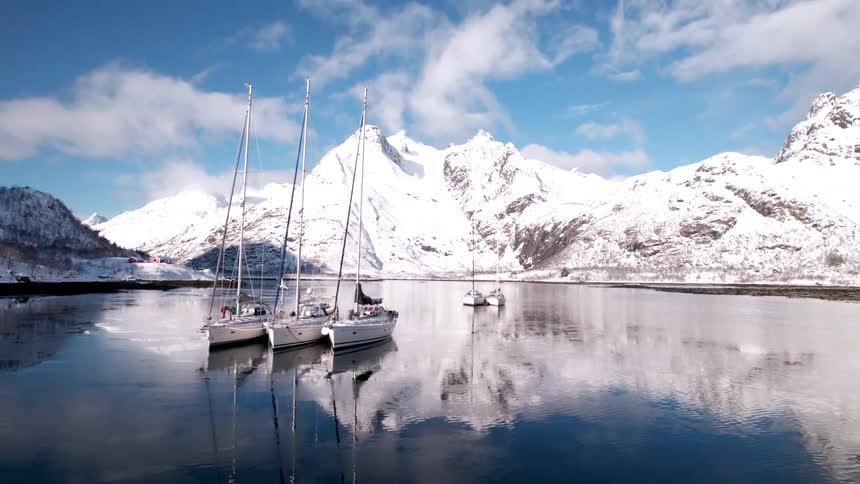 A few boats docked in the middle of a lake near some snowy mountains