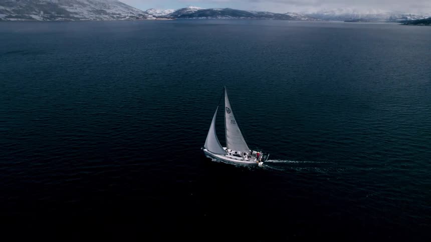 Sailing boat on a vast sea surrounded by snowy mountains