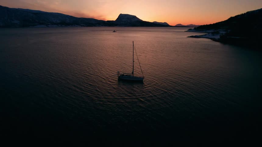 A single boat is anchored in the dark water at sunset