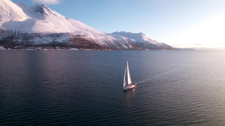 Sailboat on calm water with snowy mountains behind