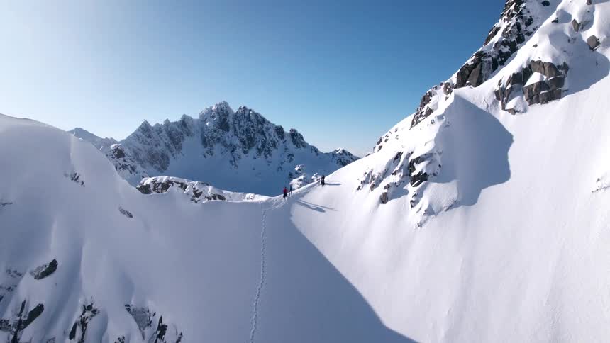 The video features a stunning highangle view of a snowcovered mountain landscape with a person standing on a ridge overlooking the vast pristine terrain distant peaks are visible under a bright clear blue sky emphasizing the immense scale of the en