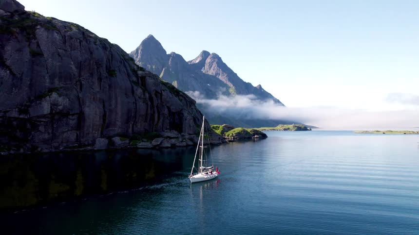 Sailboat traveling across the ocean with mountains in the background