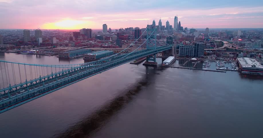 Traffic crosses a bridge near the marina while the sun shines across the city from the red tinted horizon