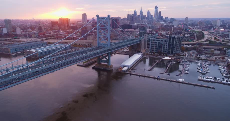 Erial view of a suspension bridge leading into a city skyline at sunset