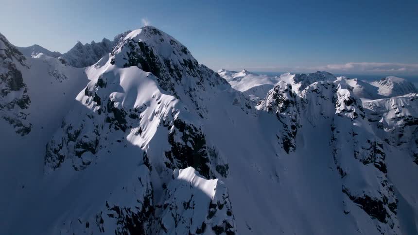 Snow covered mountains rise sharply under a clear blue sky