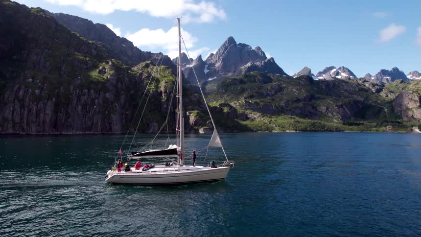 A sailboat cruises through a lake surrounded by mountains at midday