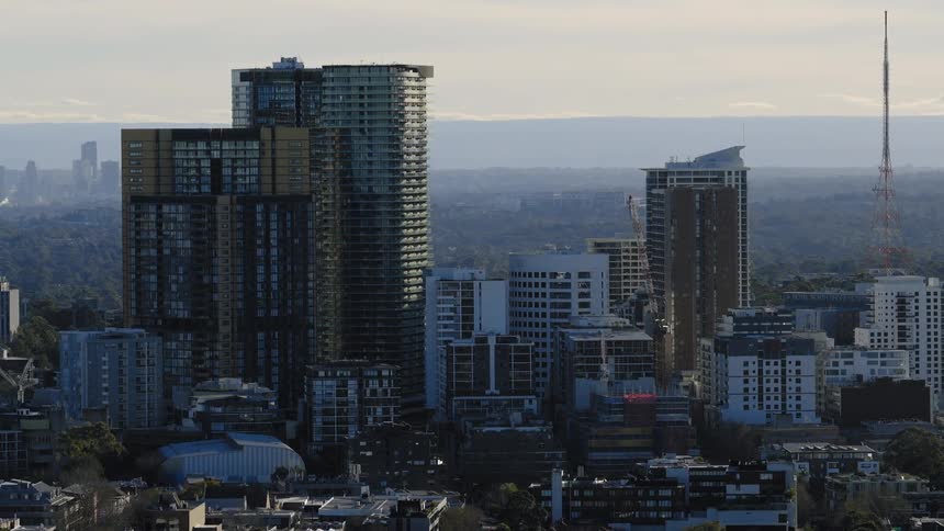 A dense cluster of modern highrise buildings dominates the city skyline with distant haze and layered urban sprawl beyond