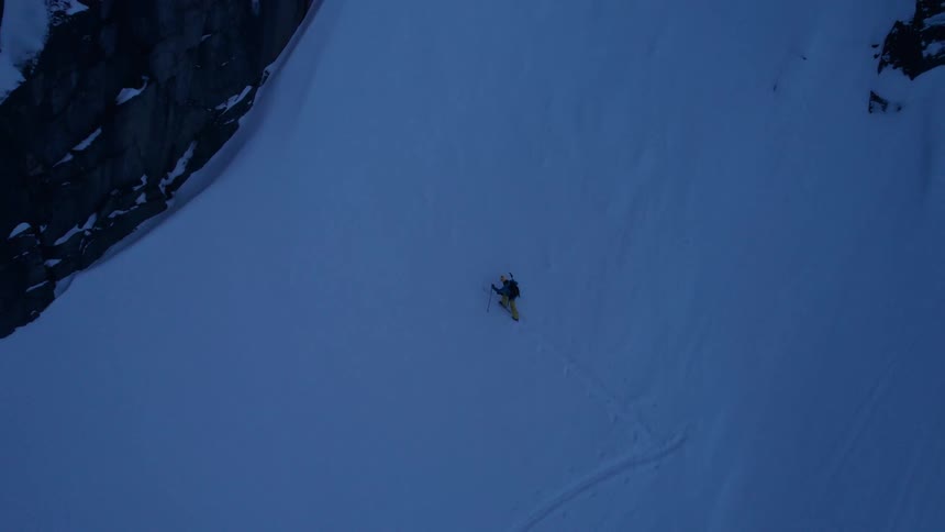 A hiker treks along a snowy mountain trail below rugged cliffs