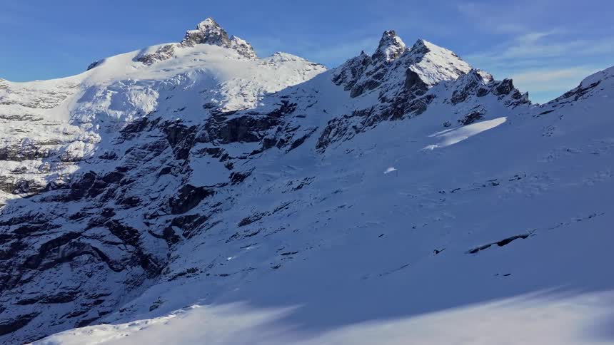 Snowcovered peaks tower under a crisp blue sky with rugged ridgelines casting sharp shadows across the alpine slope