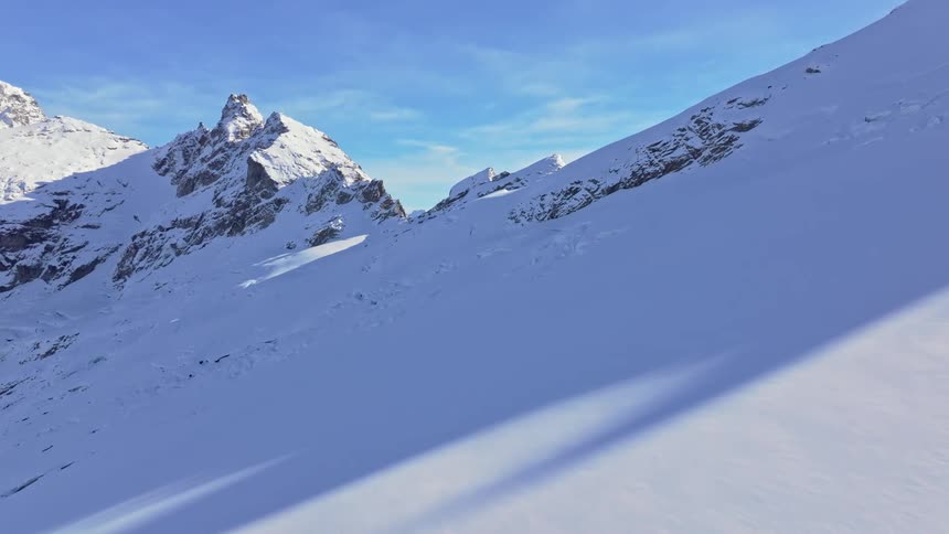 A serene snowcovered mountain landscape stretches beneath a clear blue sky with jagged peaks casting long shadows across the pristine slope