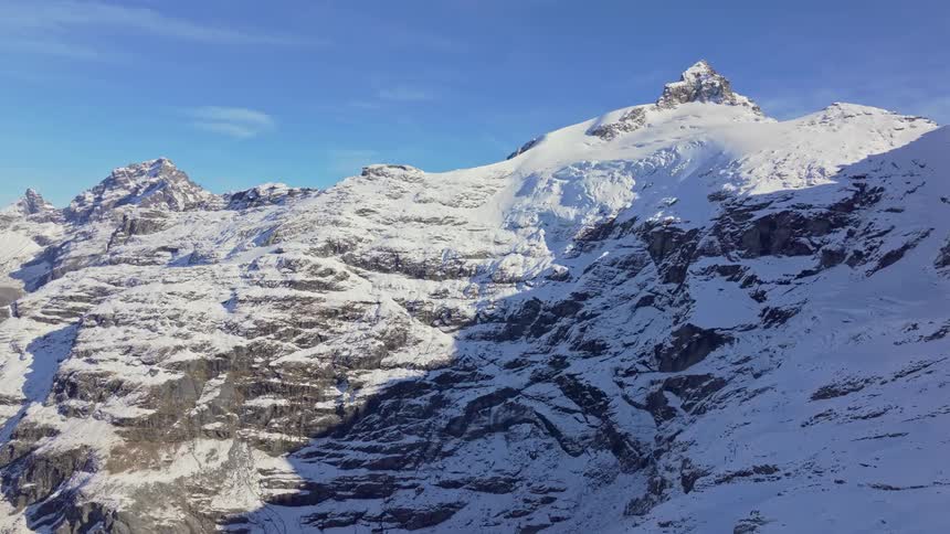 The rugged mountain face is dusted with snow and illuminated by warm sunlight on the upper peak under a clear sky