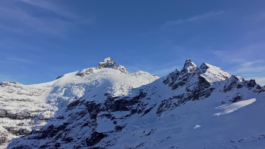 Jagged snowcovered peaks rise sharply under a vibrant blue sky their rocky faces casting bold shadows across the alpine slopes