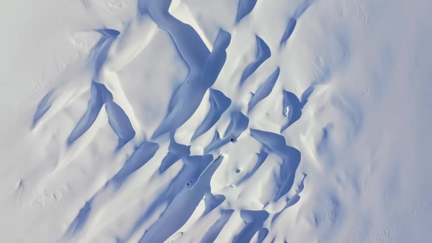 The video displays a striking abstract pattern of white and blue shapes resembling snow dunes or waves possibly captured from a high aerial perspective the interplay of light and shadow creates depth with the white areas brightly illuminated and the b
