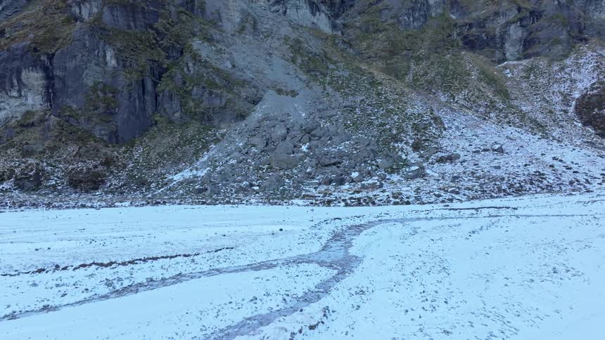 The video shows a snowcovered mountain valley with towering rugged cliffs and peaks on either side a small stream or path winds through the snow in the foreground