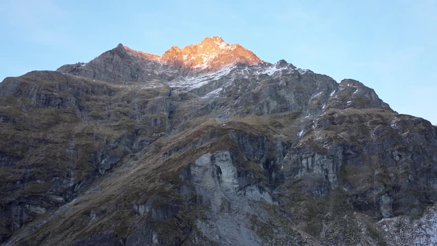 A rugged mountain peak is illuminated by golden sunlight against a clear blue sky