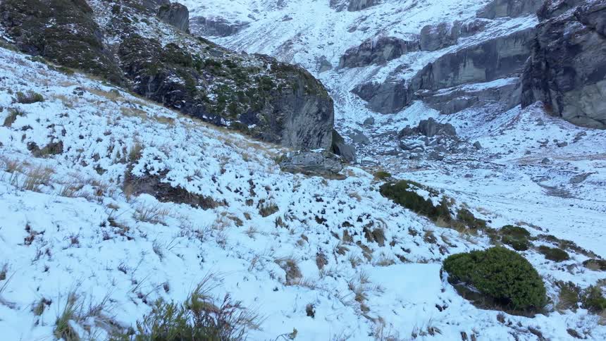 Golden light strikes the summit of a towering rugged mountain revealing steep rock faces dusted with snow beneath a clear morning sky